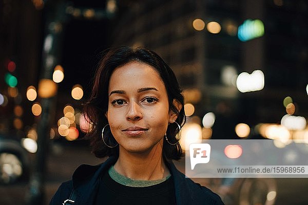 Porträt einer lächelnden Frau  die nachts in einer beleuchteten Stadt steht