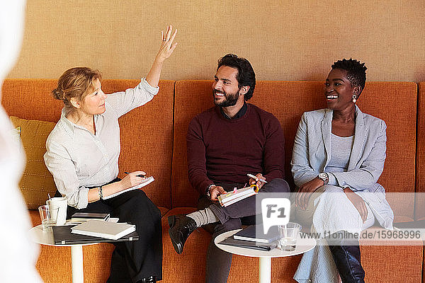 Unternehmerin diskutiert mit Geschäftsmann und Geschäftsfrau  während sie am Arbeitsplatz auf dem Sofa sitzt