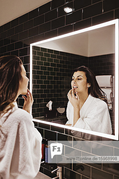 Mittelgroße erwachsene Frau schaut in den Spiegel  während sie im Hotel Lippenbalsam aufträgt