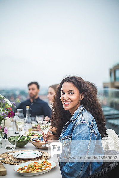 Porträt einer lächelnden Frau  die mit Freunden während eines geselligen Beisammenseins auf dem Dach sitzt