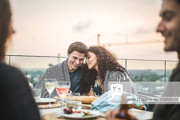 Lächelnder Mann und lächelnde Frau sitzen bei Sonnenuntergang mit Decke auf der Terrasse