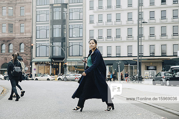 Porträt einer Unternehmerin in Jacke beim Überqueren der Straße in der Stadt