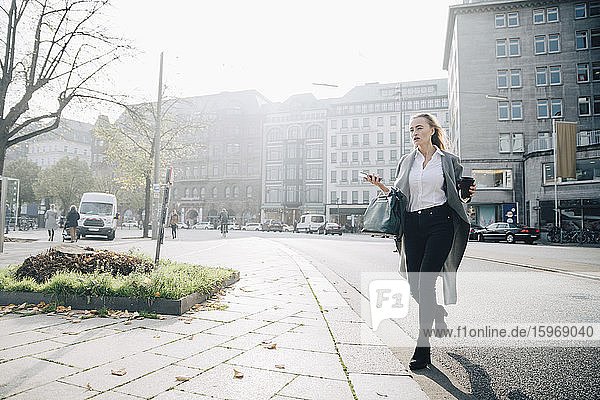 Full length of female entrepreneur with smart phone walking in city