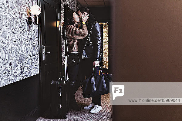 Seitenansicht eines Paares  das sich am Eingang des Hotelzimmers küsst