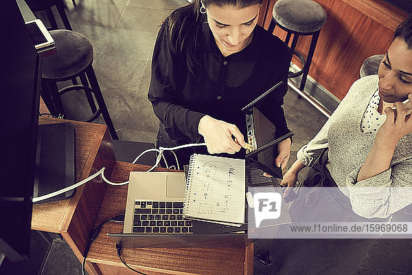 Hochwinkelansicht des Eigentümers  der das Kabel im Modem einstellt  während ein Kollege im Café über ein Smartphone spricht