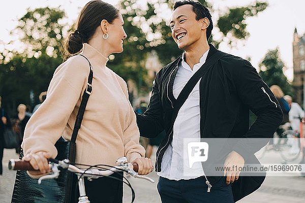 Lächelnde Frau mit Fahrrad schaut einen Freund an  während sie in der Stadt steht