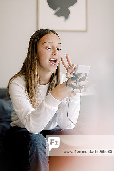 Teenagermädchen  die zu Hause sitzend Selbsthilfe per Mobiltelefon nimmt