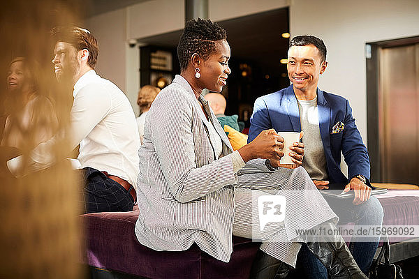 Smiling female and male business people communicating while sitting in office seminar
