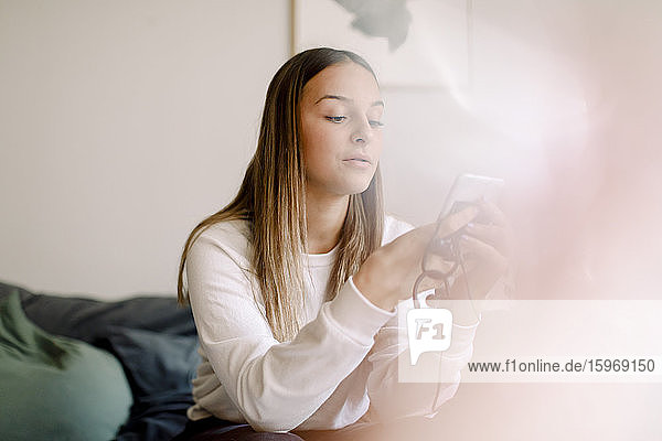 Teenagerin nutzt soziale Medien auf Smartphones  während sie zu Hause sitzt