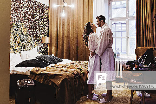 Seitenansicht eines romantischen Paares  das sich umarmt  während es im Hotelzimmer am Bett steht