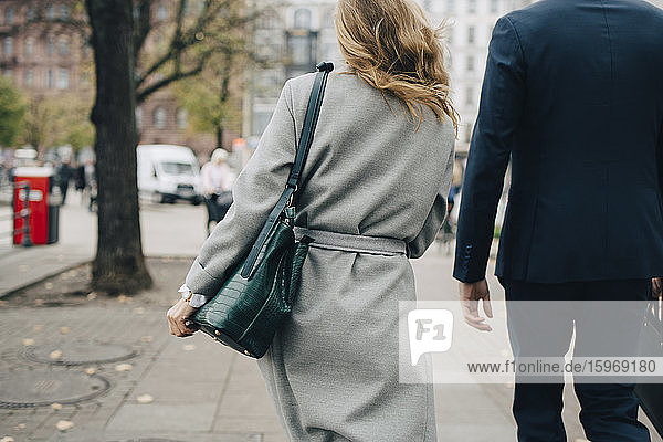 Rear view of businesswoman with handbag walking by colleague in city