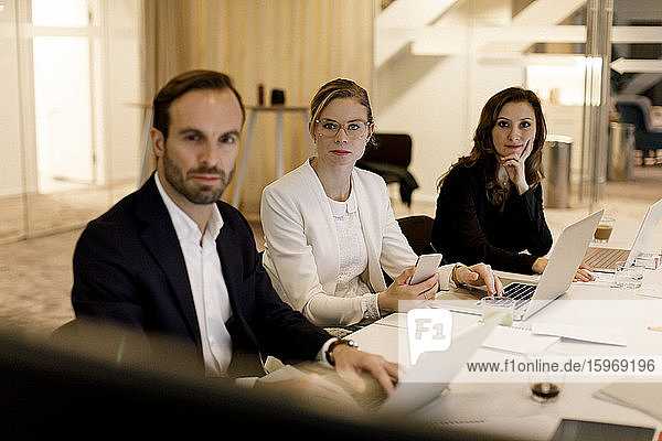 Männliche und weibliche Berufstätige im mittleren Erwachsenenalter  die bei Besprechungen zuhören  während sie im Büro am Konferenztisch sitzen
