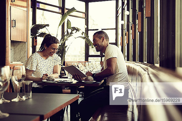 Lächelnder Mann und lächelnde Frau mit digitalem Tablett sitzen am Tisch im Café