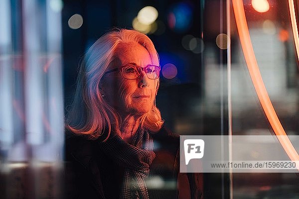 Verschrumpelte Frau schaut weg  während sie nachts in der Stadt steht