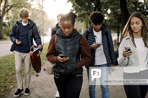 Multi-ethnic teenage friends using smart phones while walking on street in city