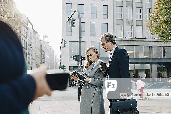 Business colleagues looking in book while standing in city