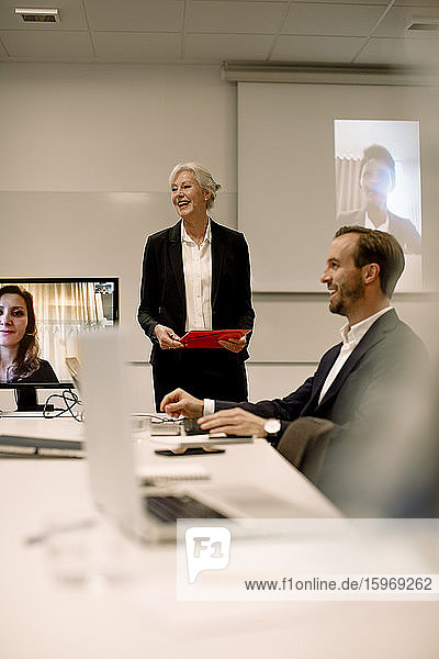 Smiling mature professional discussing with colleagues in video conference at board room