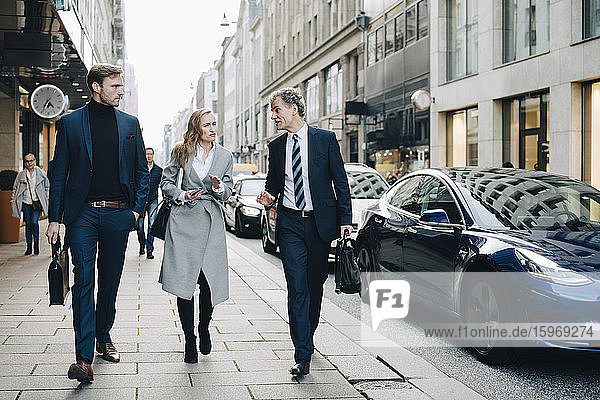 Geschäftsfrau mit männlichen Kollegen gehen in der Stadt auf dem Bürgersteig