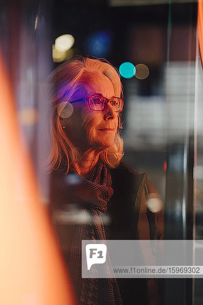 Ältere Frau schaut weg  während sie nachts in der Stadt steht