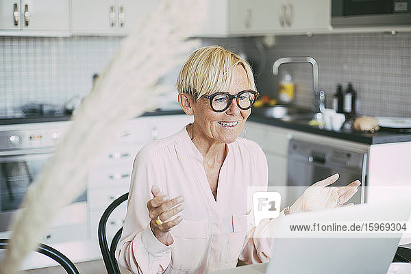 Frau in der Küche mit einer Online-Besprechung  die zu Hause arbeitet