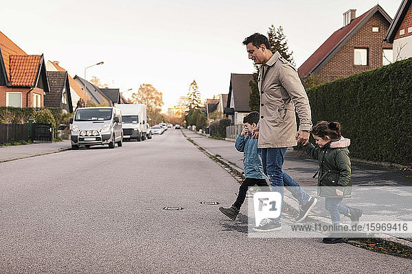 Vater überquert im Herbst mit Kindern den Fußweg
