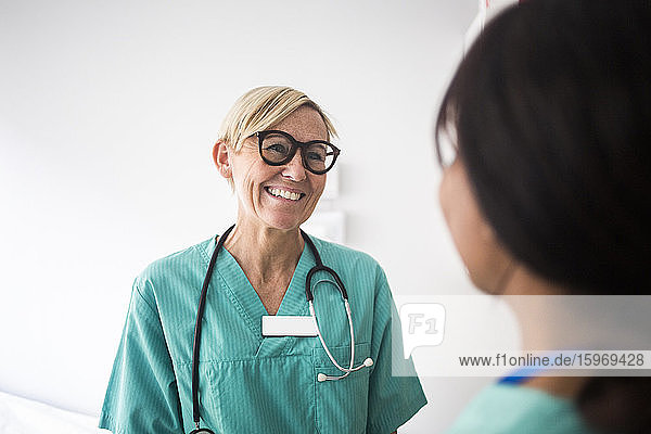 Lächelnder reifer Kinderarzt im Gespräch mit weiblicher Mitarbeiterin im Stehen in der Klinik