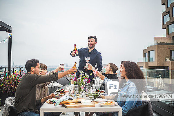 Junger Mann trinkt mit Freunden während eines geselligen Beisammenseins auf dem Dach