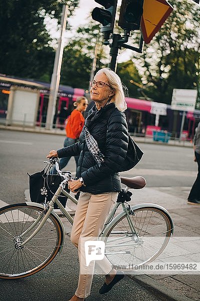 Senior woman with bicycle crossing road in city