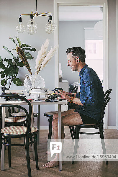 Happy man sitting at table in underwear working at home having a video call