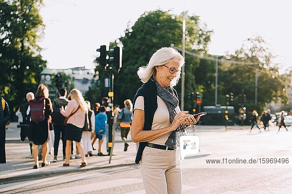 Lächelnde  faltige Frau mit Smartphone auf der Straße in der Stadt