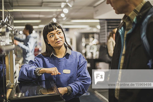 Verkäuferin sieht reifen Kunden an  während sie im Elektronikgeschäft steht