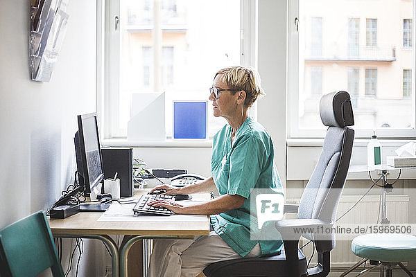 Seitenansicht einer reifen Ärztin  die in der Klinik am Computer arbeitet