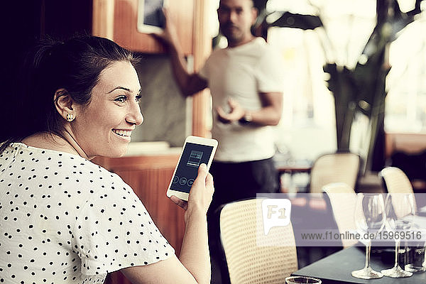 Rückansicht einer lächelnden Frau mit Smartphone  die wegschaut  während ein Mann im Cafe steht