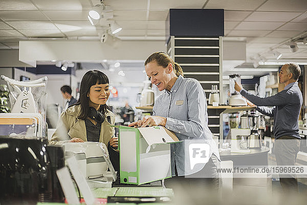 Mature female owner showing appliance to young customer in electronics store
