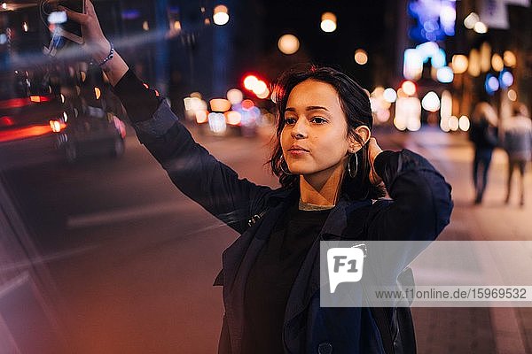 Junge Frau mit Hand in den Haaren  die nachts in der Stadt nach einem Taxi ruft