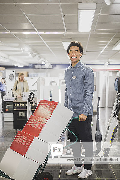 Porträt eines lächelnden männlichen Besitzers mit Gepäckwagen im Elektronikladen