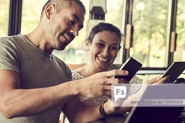 Lächelnder Mann zeigt der Partnerin im Café ein Smartphone