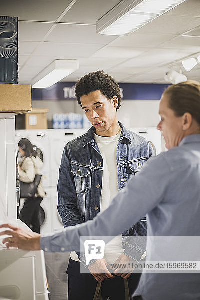 Mature owner explaining about washing machine to male customer in electronics store