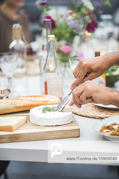 Cropped hands of man cutting mozzarella over cutting board at building terrace during party