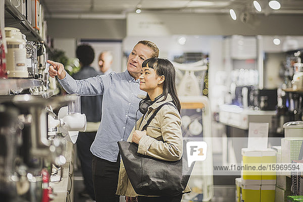 Mature female owner pointing at appliance to young customer in electronics store
