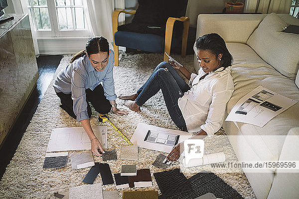 High angle view of female designers discussing about fabric swatch while sitting on carpet at home office