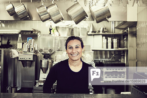 Portrait of smiling owner standing at checkout counter in cafe