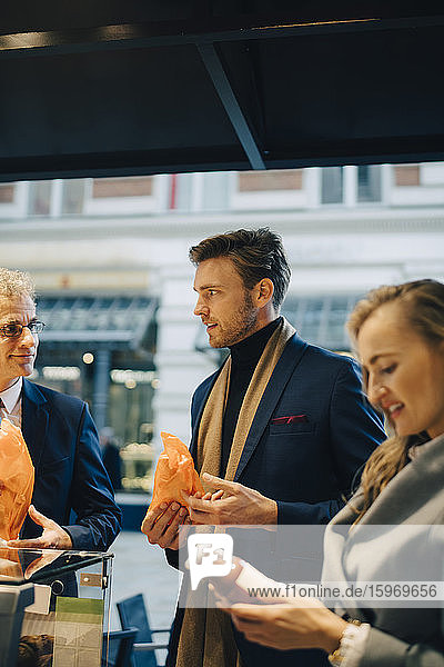 Business people discussing while holding food and drink in city