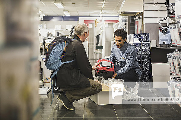 Smiling young salesman showing appliance to male customer in store