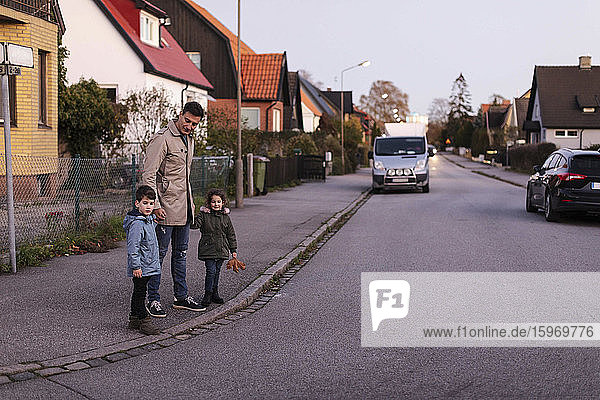Vater steht im Herbst mit Kindern auf dem Bürgersteig