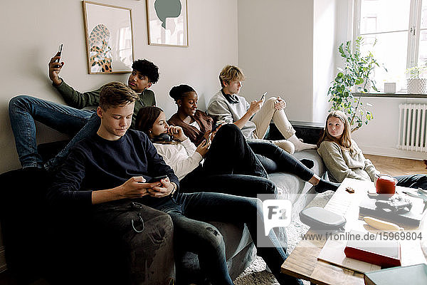 Mädchen und Jungen im Teenageralter benutzen zu Hause im Wohnzimmer Smartphones