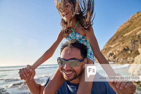 Happy father carrying daughter on shoulders on sunny beach