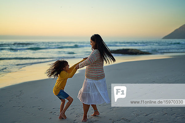 Glückliche Mutter und Tochter drehen sich bei Sonnenuntergang am Meeresstrand