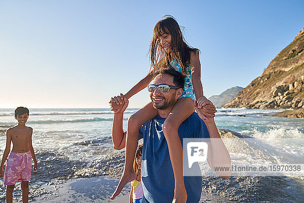 Glücklicher Vater trägt Tochter auf den Schultern am sonnigen Meeresstrand