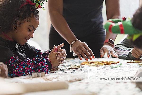 Girl decorating Christmas cookies with family at table